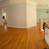 Empty hardwood-floored room with white walls and a staircase railing on the right
