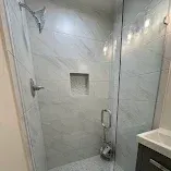 Walk-in shower with gray tiled walls, glass door, built-in niche, and handheld showerhead.