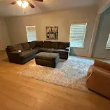 Living room with gray sectional sofa, ottoman, white shag rug, and hardwood floors between two windows.