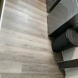 Light wood flooring beside a dark cabinet or appliance near a wall corner