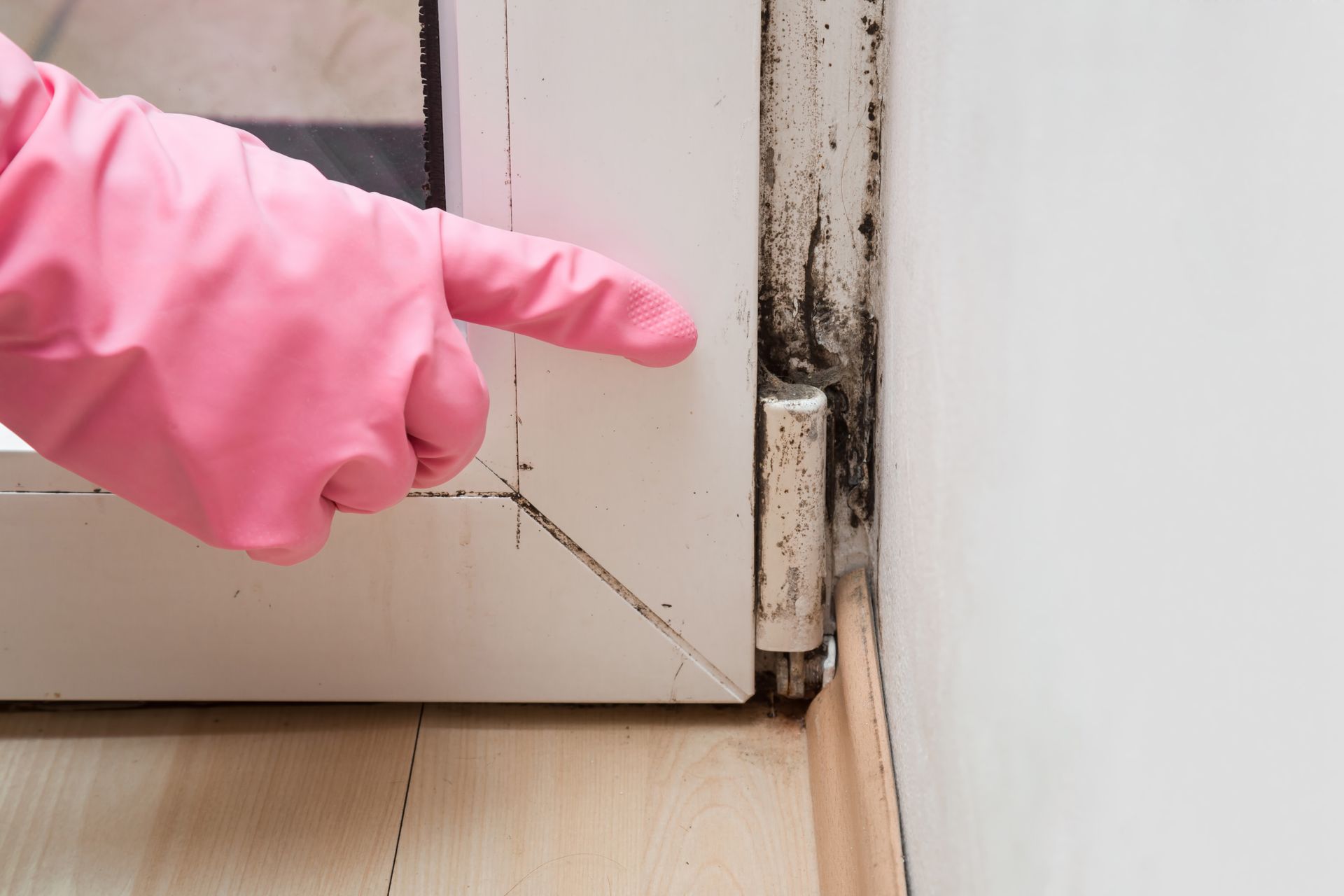 Pink-gloved hand pointing at a damaged door hinge and gap in a white door frame Pink-gloved hand pointing at a damaged door hinge and gap in a white door frame