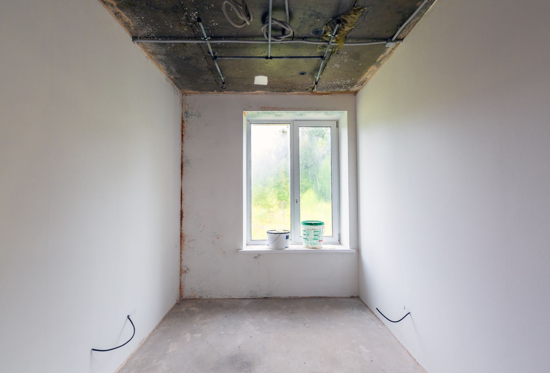Empty unfinished room with white walls, exposed ceiling, and a window at the far end.