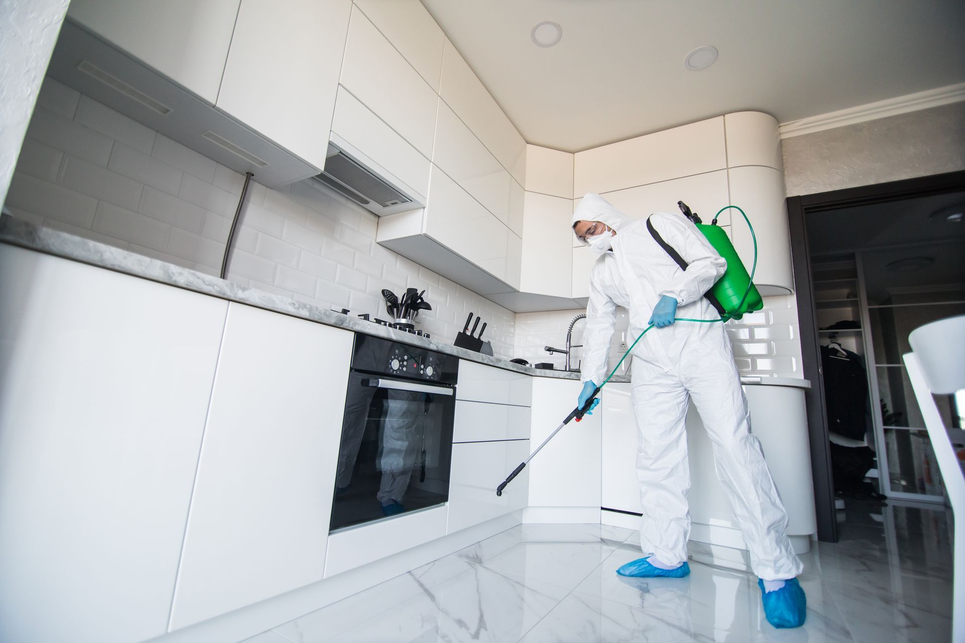 Worker in white protective suit disinfecting a modern kitchen with a spray wand Worker in white protective suit disinfecting a modern kitchen with a spray wand