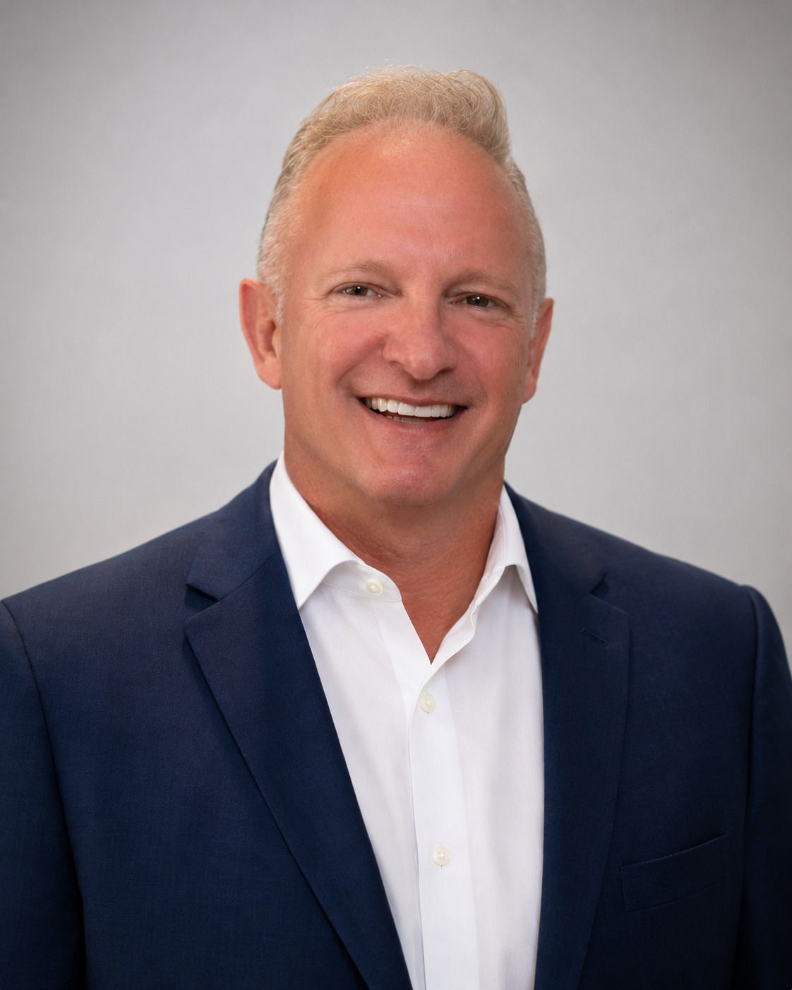 Smiling person in a navy blazer and white shirt against a gray background Smiling person in a navy blazer and white shirt against a gray background
