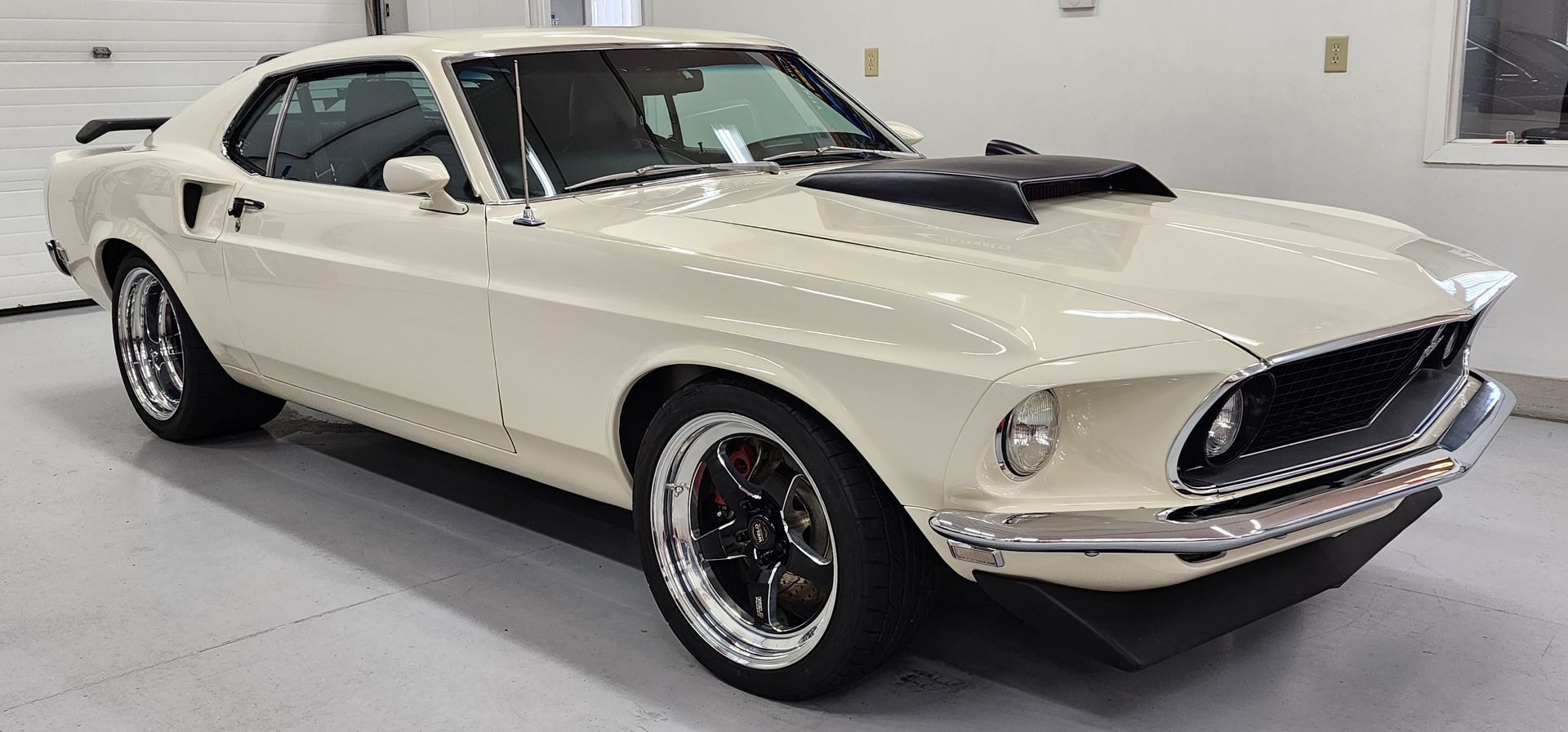Cream-colored 1969 Ford Mustang with black hood scoop, parked indoors.