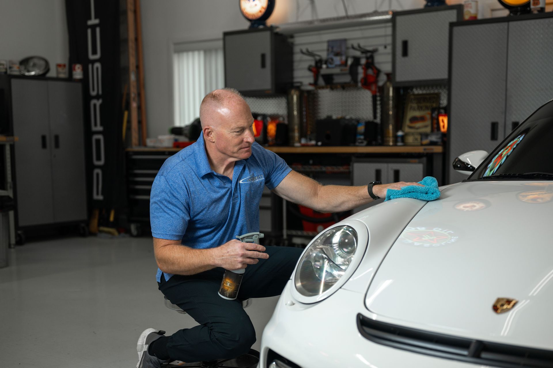 a man is kneeling down next to a white porsche in a garage .