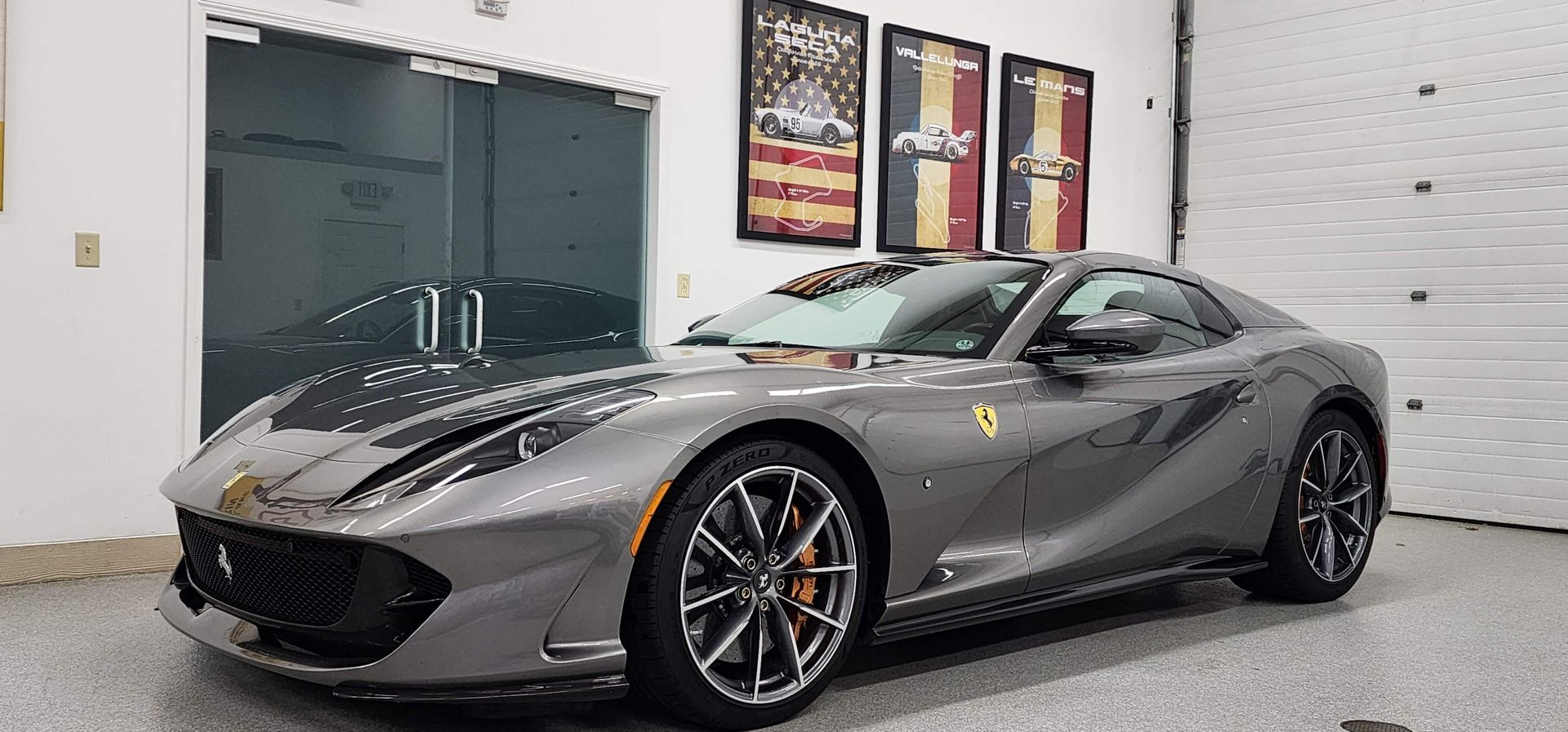 Gray Ferrari coupe parked in a garage with artwork on the wall.
