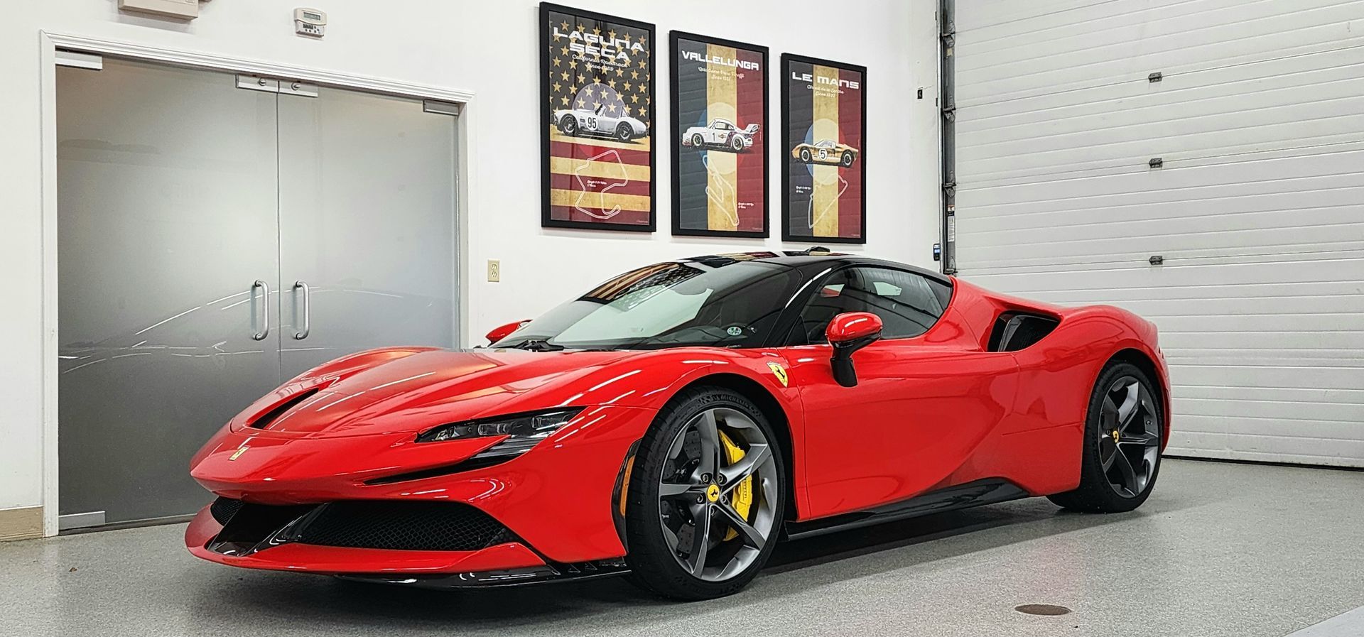 Red Ferrari SF90 sports car in a garage with art on the wall.