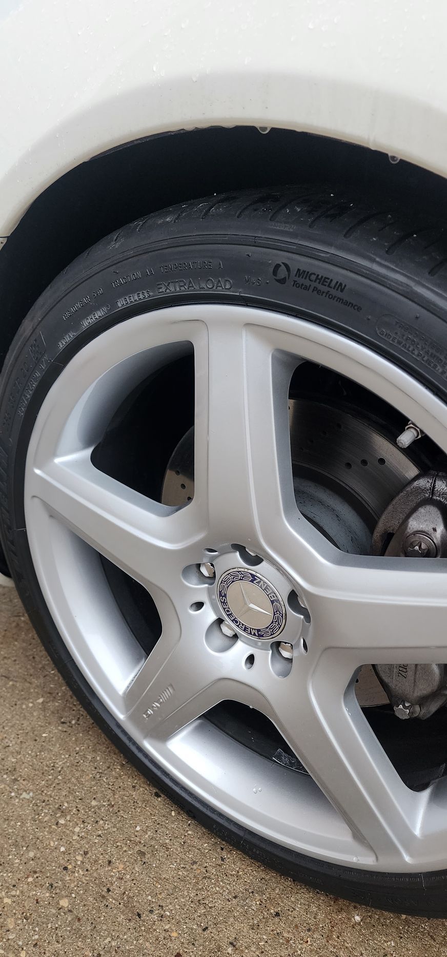 Close-up of a silver alloy wheel on a car, showing the tire, brake disc, and a white fender.