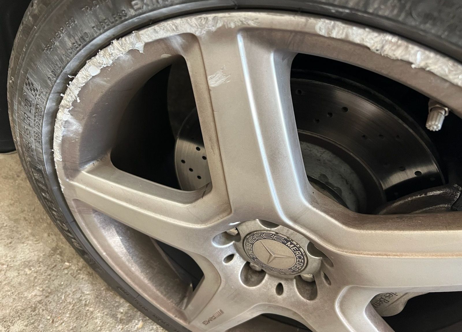 Close-up of a silver Mercedes wheel with tire and brake rotor, showing damaged paint around the rim.