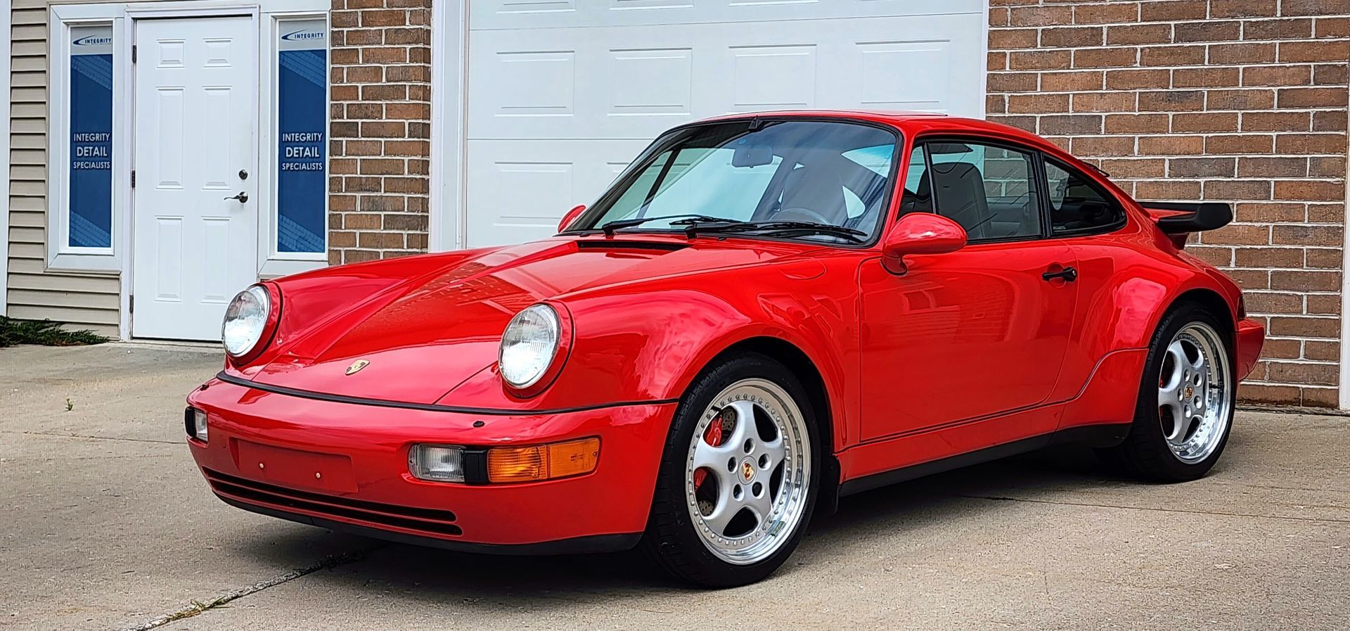 Red Porsche 911 parked in front of a garage. Shiny red paint and silver rims.