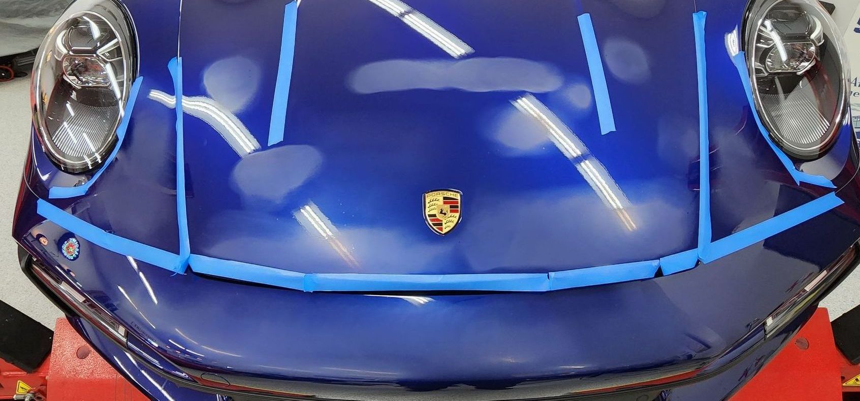 Blue Porsche car hood with tape, ready for detailing.