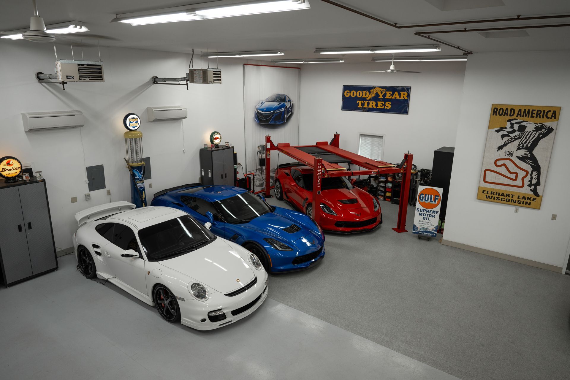 Garage with three sports cars: white, blue, red; a car lift, and vintage decor.