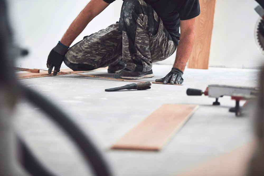 a man is kneeling down on the floor cutting a piece of wood .