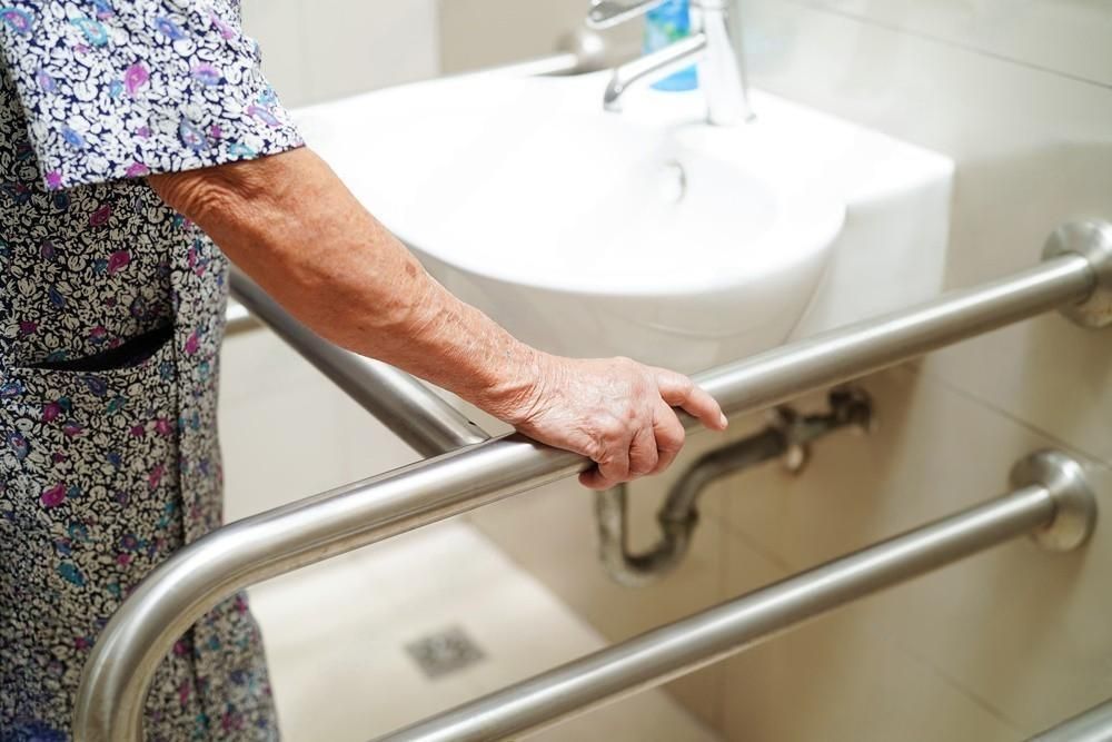 an elderly woman is holding onto a stainless steel railing in a bathroom .