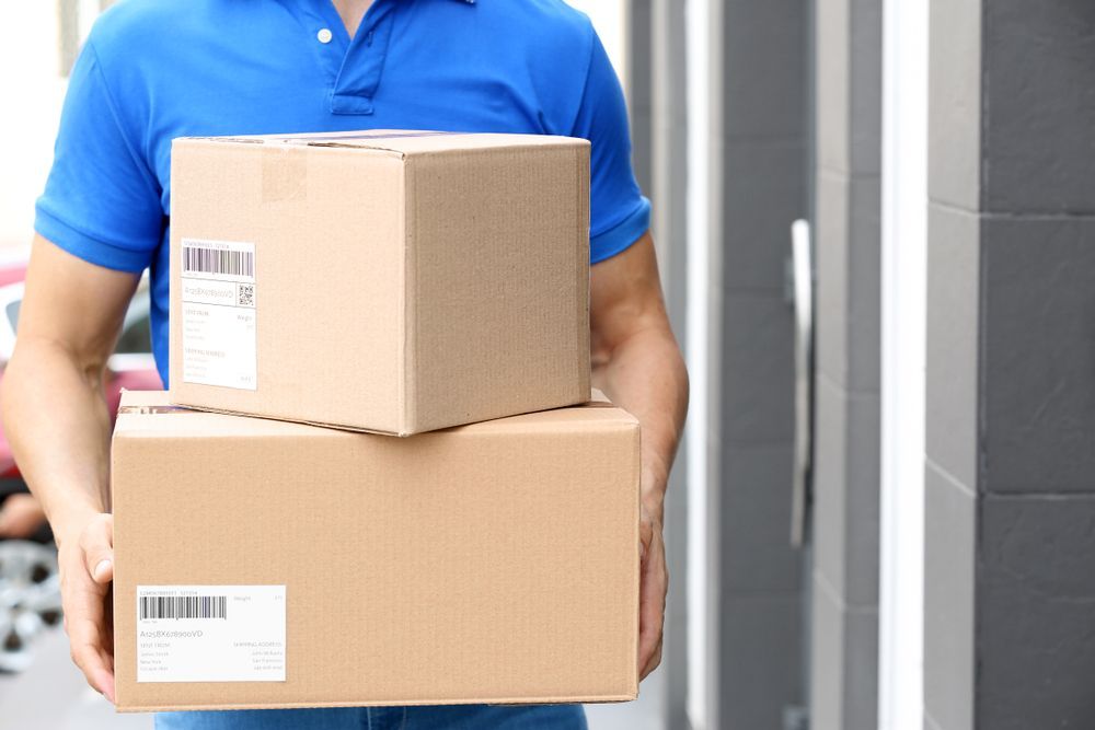 A Delivery Man Is Holding A Stack Of Boxes In His Hands — James Fast Freight in Wagga Wagga, NSW