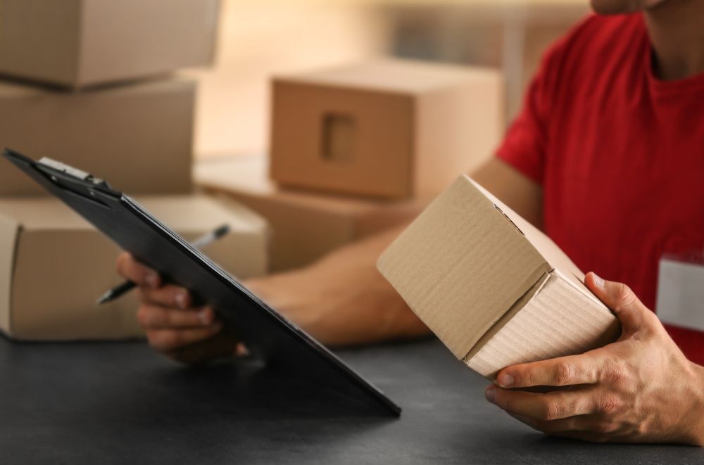 A Delivery Man Is Holding A Box And Looking At A Clipboard — James Fast Freight in Albury, NSW