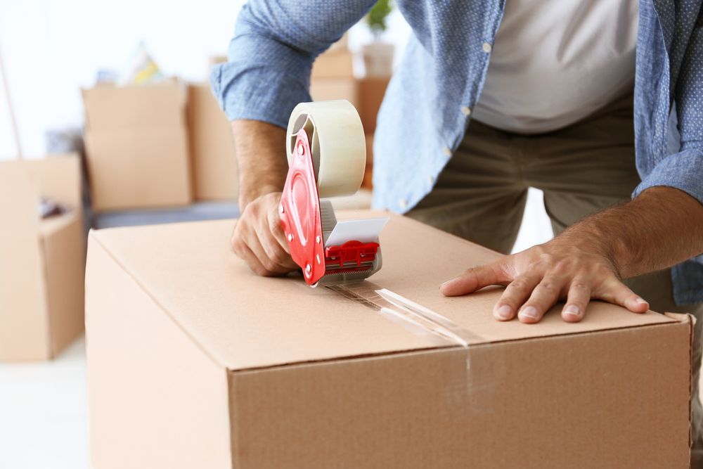 A Man Is Taping A Cardboard Box With Tape — James Fast Freight in Albury, NSW