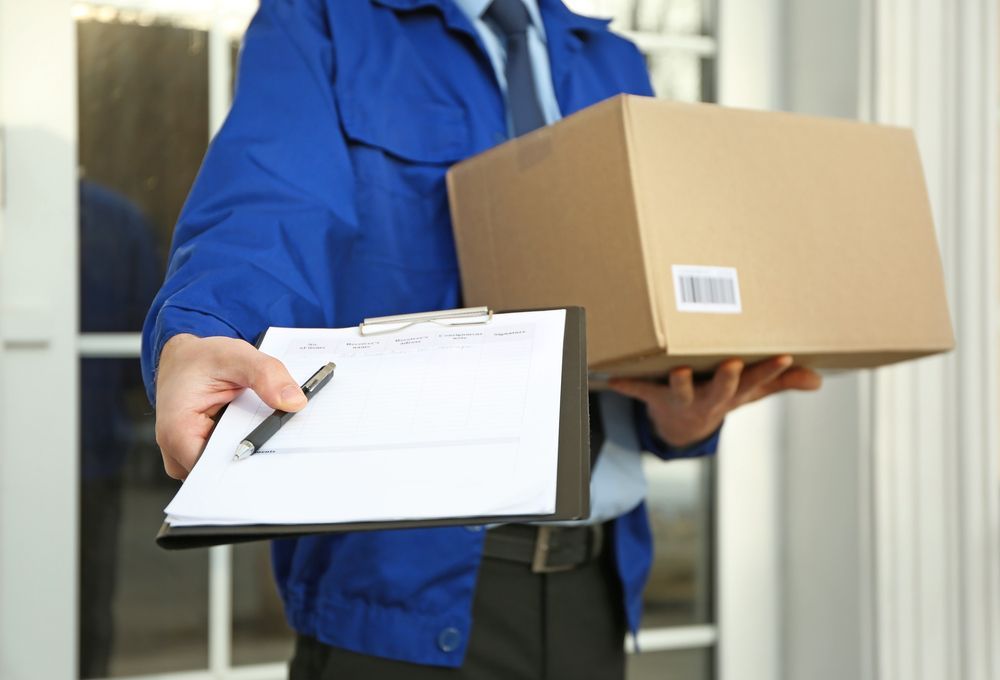 A Delivery Man Is Holding A Box And A Clipboard — James Fast Freight in Wodonga, NSW