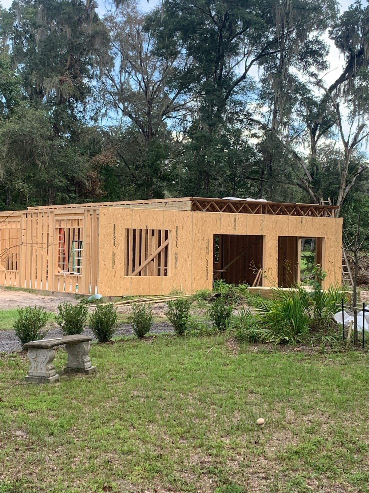A wood-framed building under construction outdoors with a garden in the foreground.