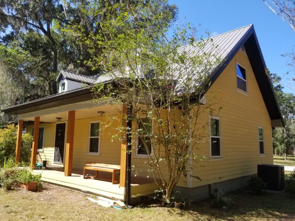 Yellow house with porch, metal roof, and a tree in front.