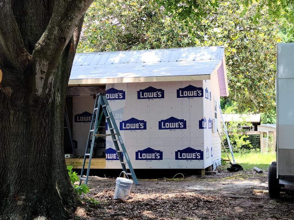 Small building under construction, wrapped in blue Lowe's paper. Ladder leans against the side.