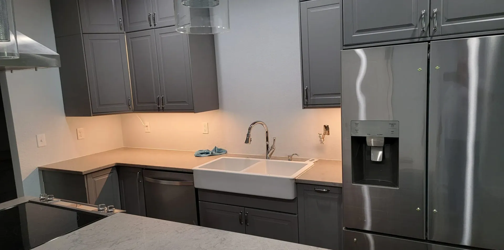 Kitchen with gray cabinets, stainless steel appliances, white farmhouse sink, and light-colored countertops.