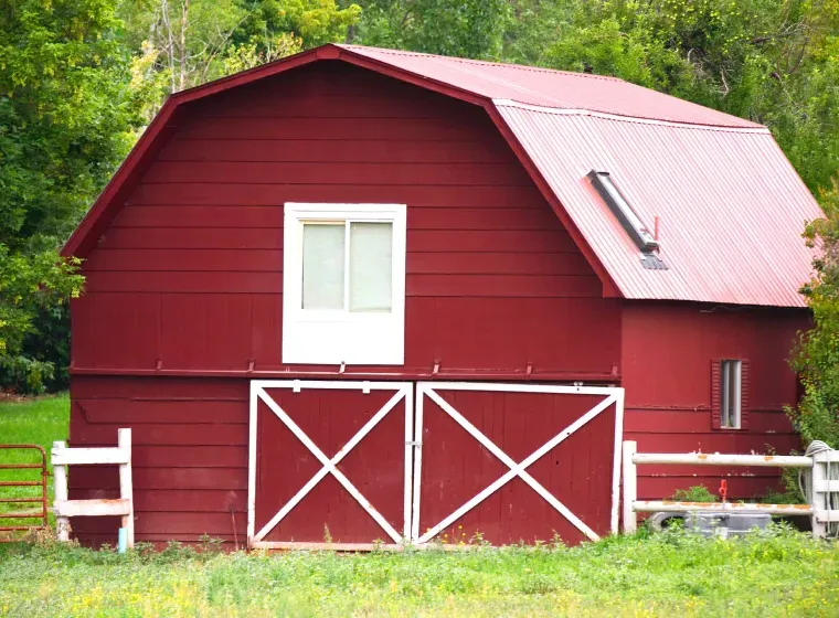 Red barn with white accents, fields, and trees.