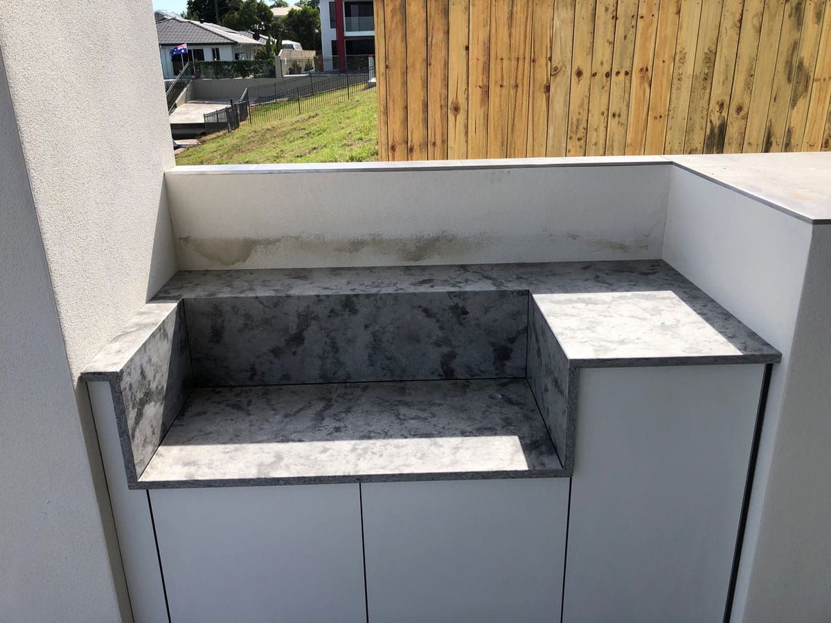 A White Cabinet With A Gray Counter Top And A Wooden Fence In The Background — Southeast Stone Pty Ltd In Noosa, QLD