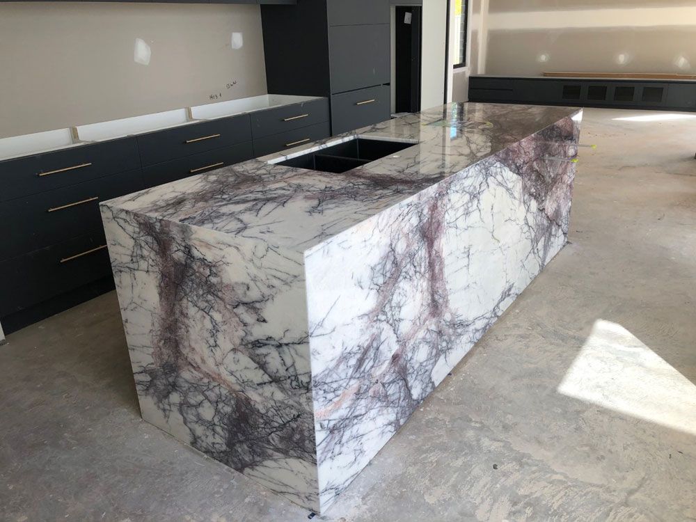 A Kitchen With A Large Marble Counter Top And Black Cabinets — Southeast Stone Pty Ltd In Gympie, QLD