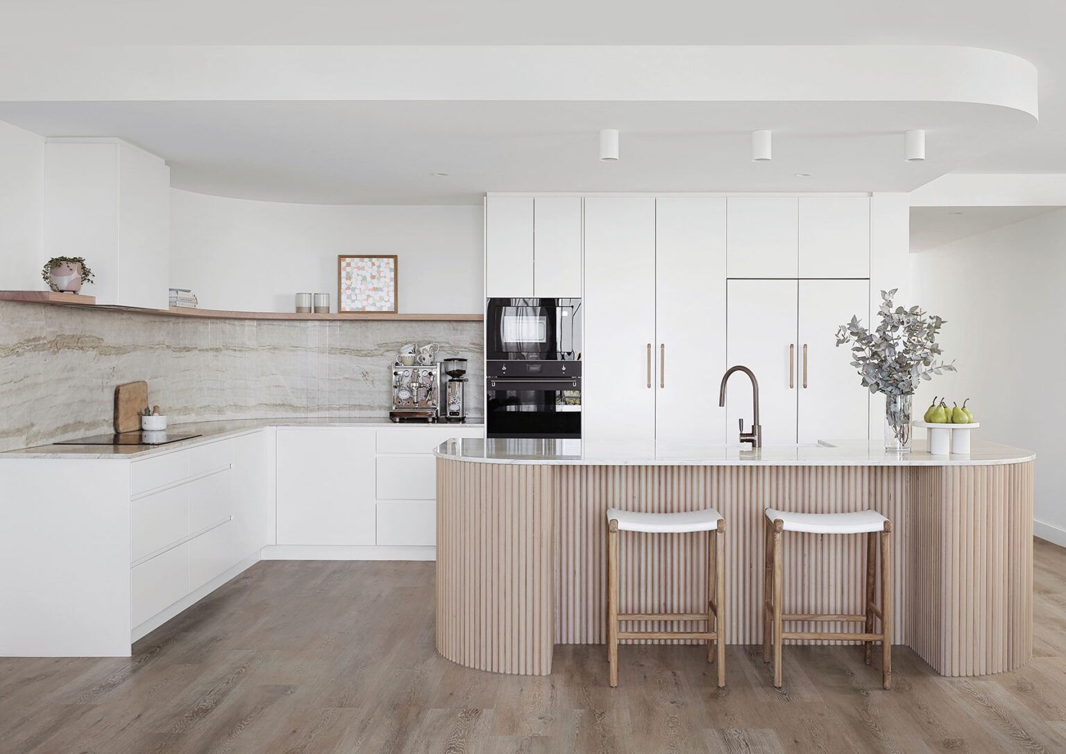 Bright modern white kitchen with wood island, two stools, black built-in oven, and pendant lights — Southeast Stone Pty Ltd In Caloundra West, QLD