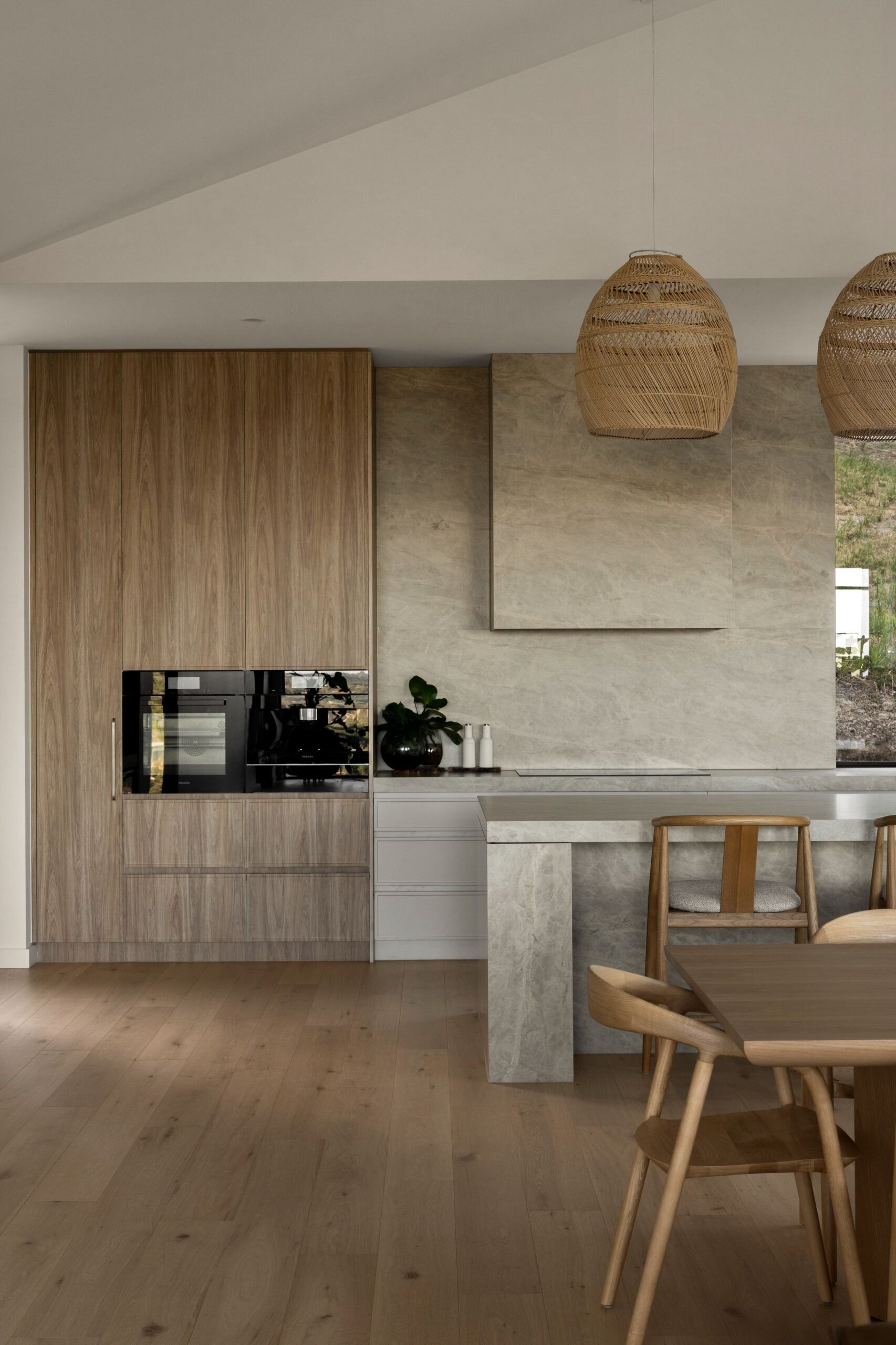 Modern kitchen and dining area with wood cabinetry, beige stone island, and woven pendant lights. — Southeast Stone Pty Ltd In Caloundra West, QLD