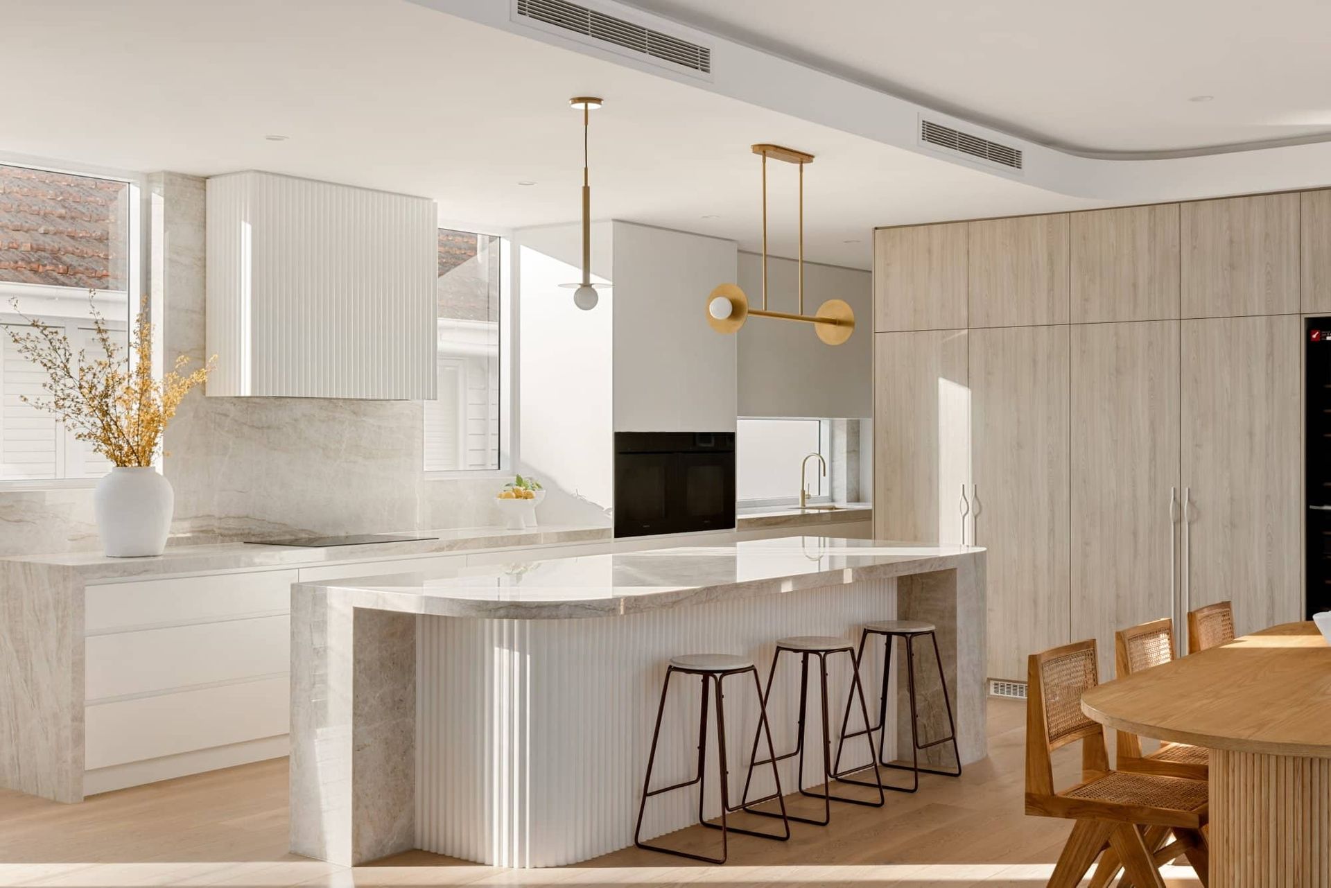 Bright modern kitchen with white cabinetry, marble island, pendant lights, and wooden stools — Southeast Stone Pty Ltd In Caloundra West, QLD