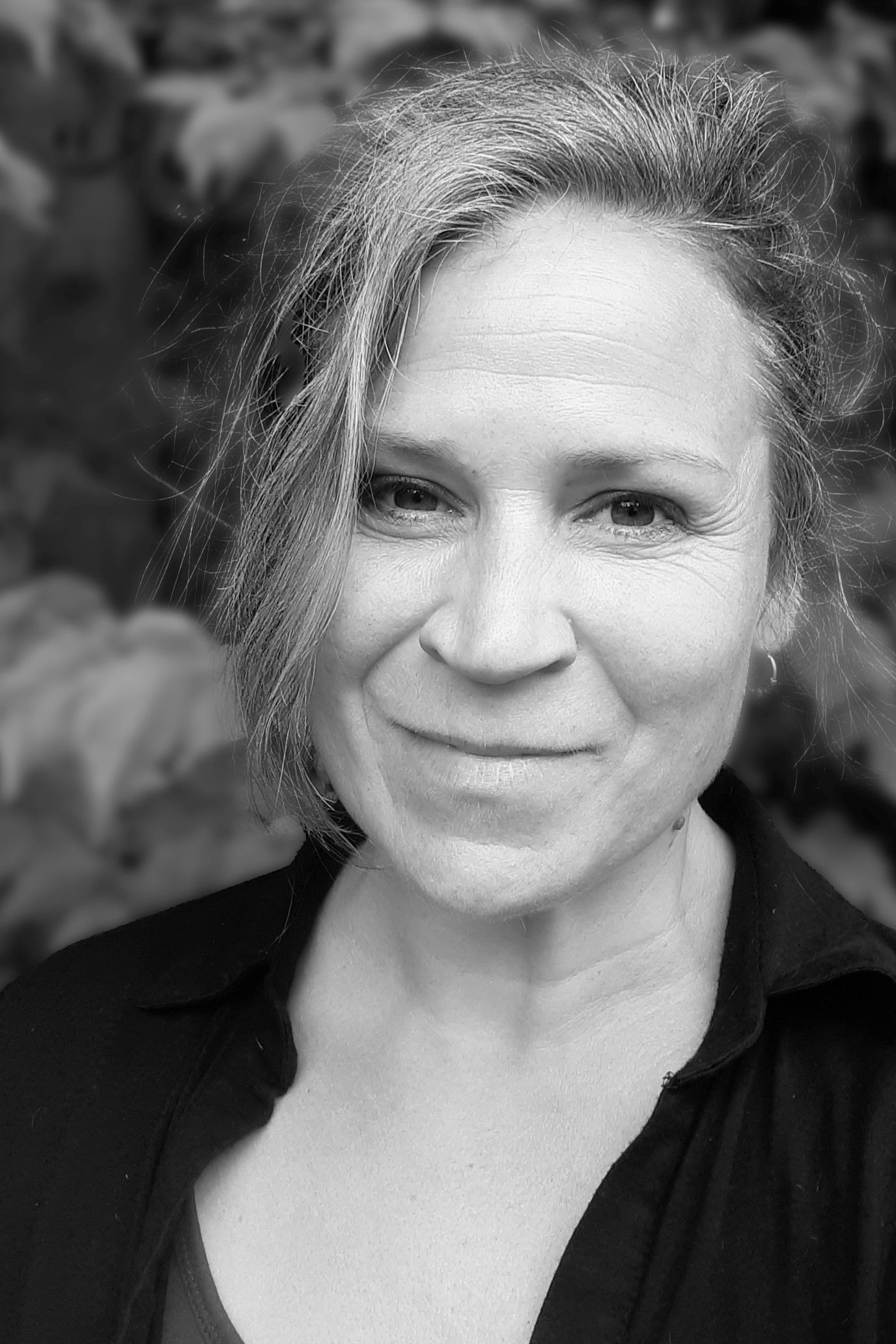 A woman in a black shirt is smiling in a black and white photo.