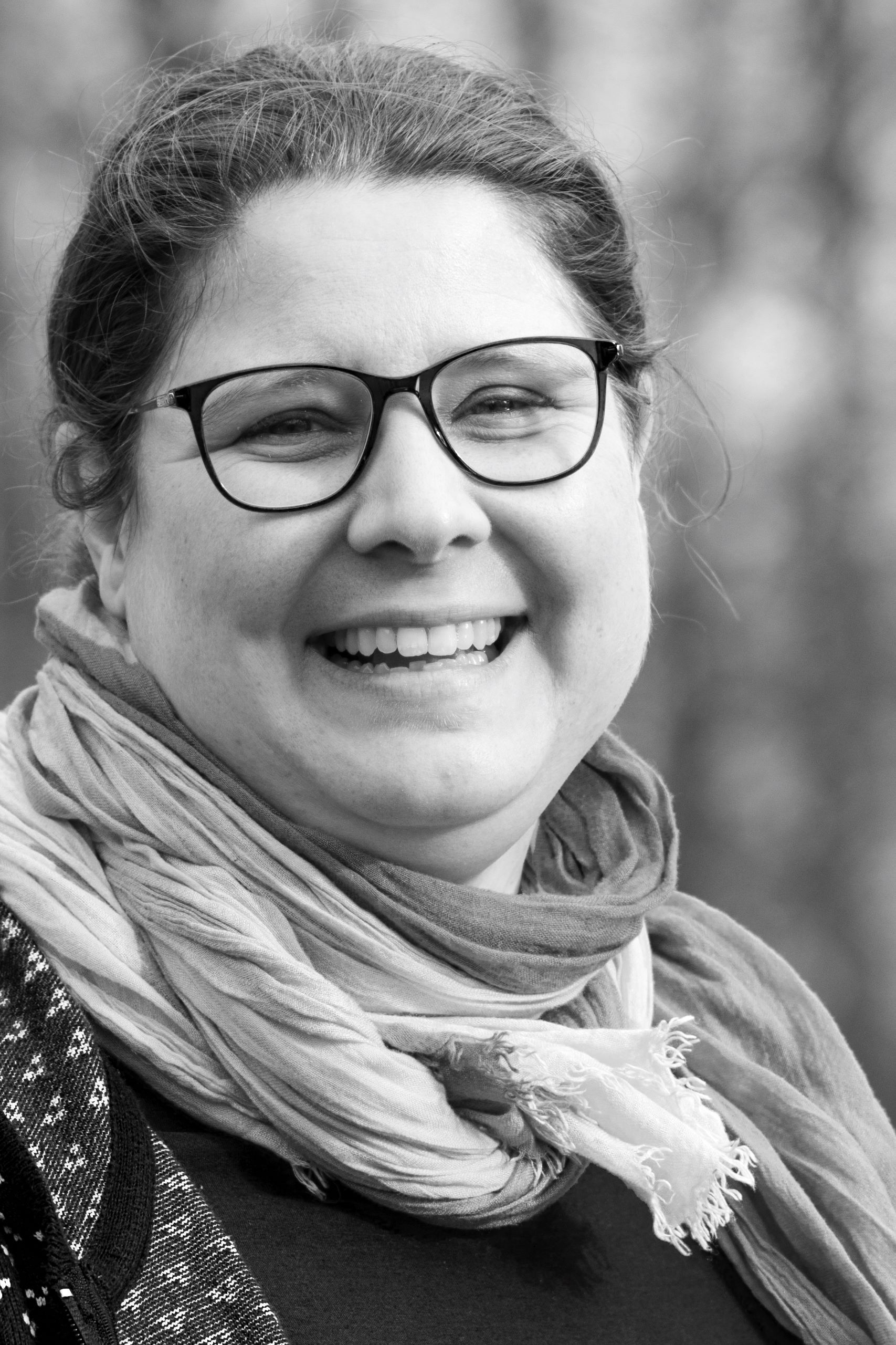 A woman wearing glasses and a scarf is smiling in a black and white photo.