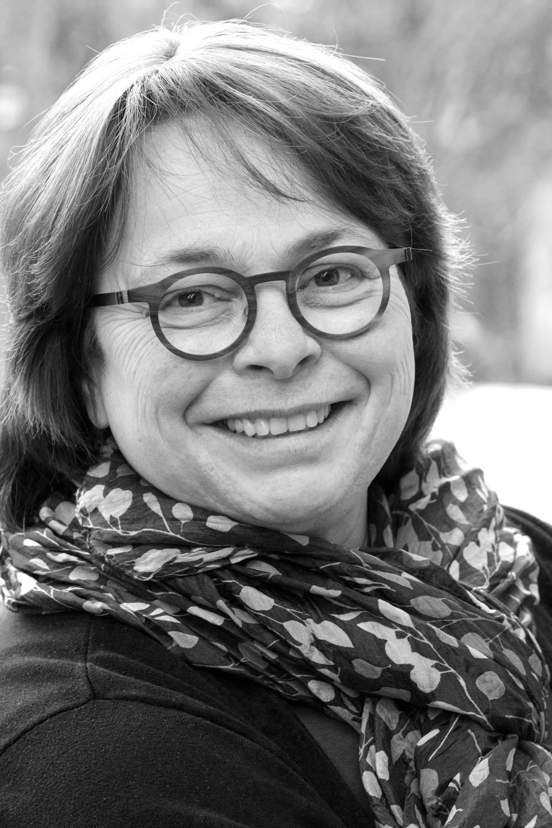 A woman wearing glasses and a scarf is smiling in a black and white photo.