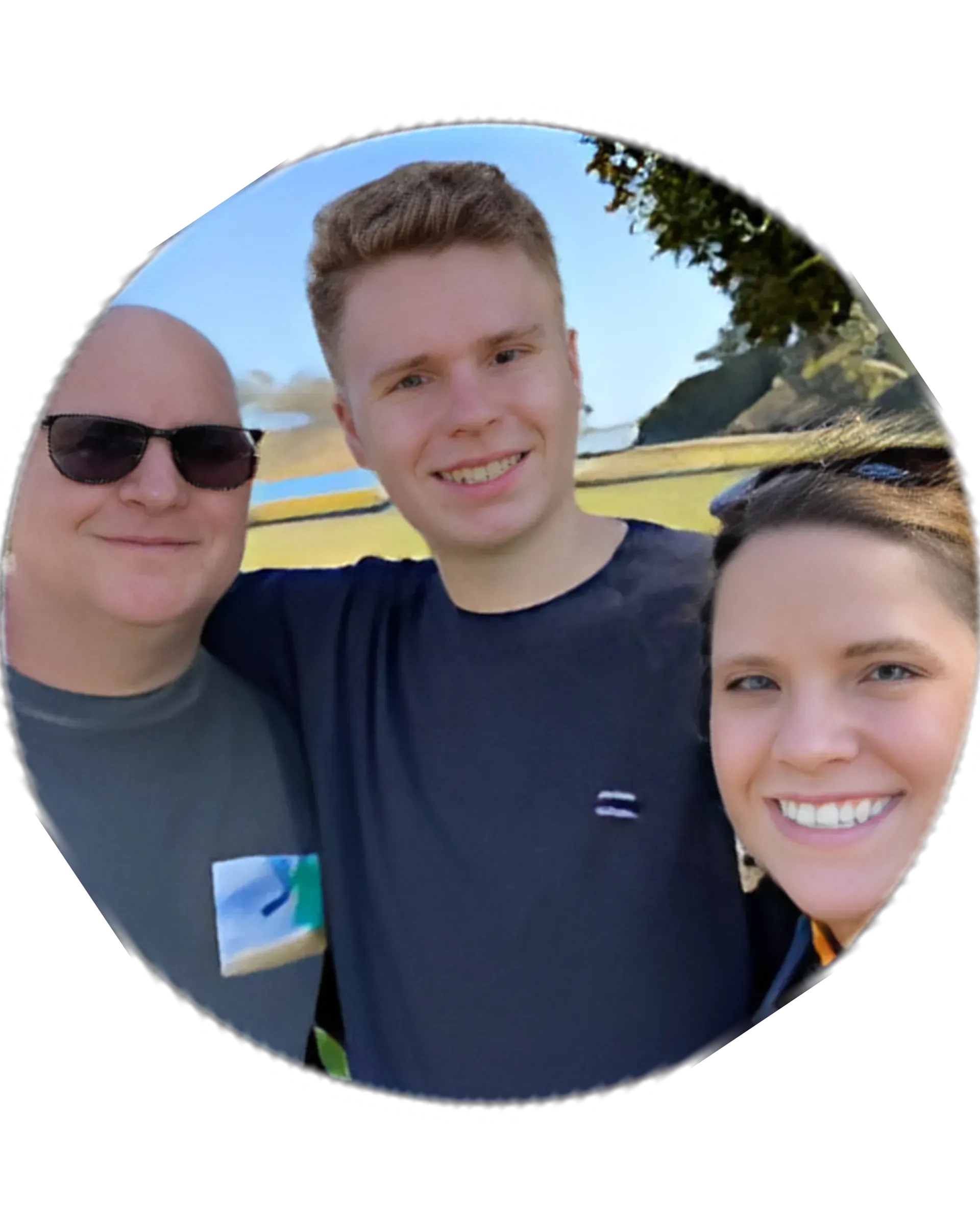 Three smiling people posing outdoors on a sunny day, with trees and a clear sky behind them.