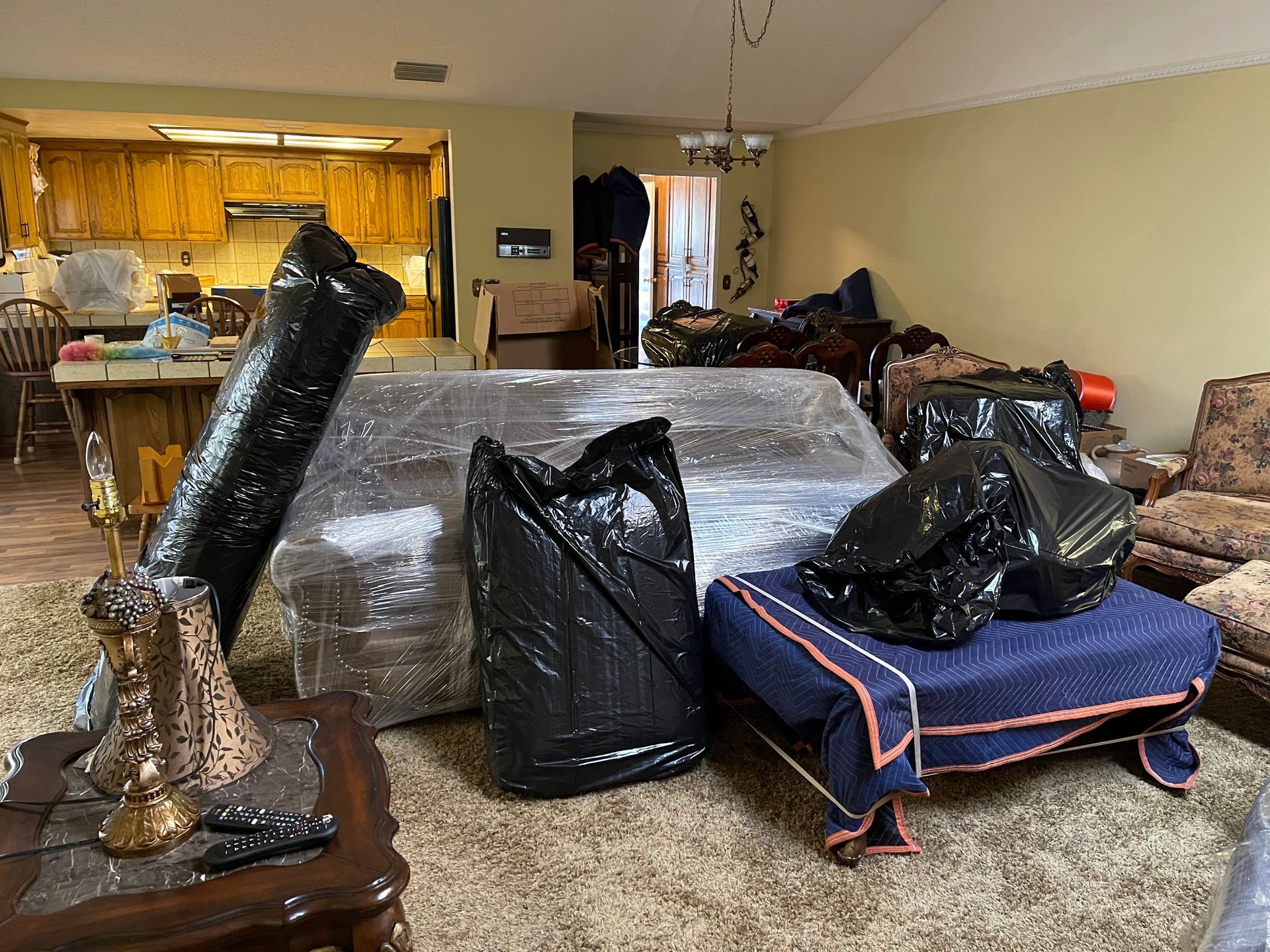 Living room filled with packed furniture, mattresses, and wrapped items, as if moving or after a flood.
