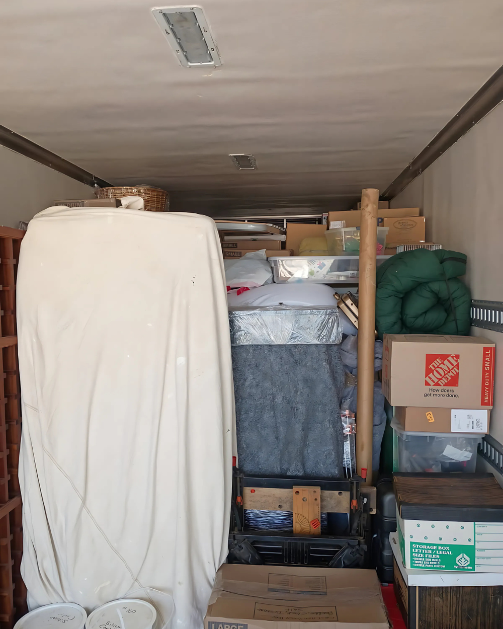 Packed storage room inside a truck trailer with boxes, wrapped furniture, and stacked household items.