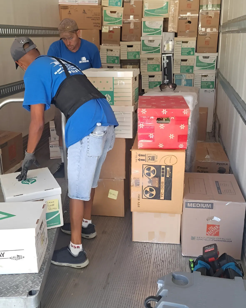 Two people loading cardboard boxes in a truck filled with packed cartons
