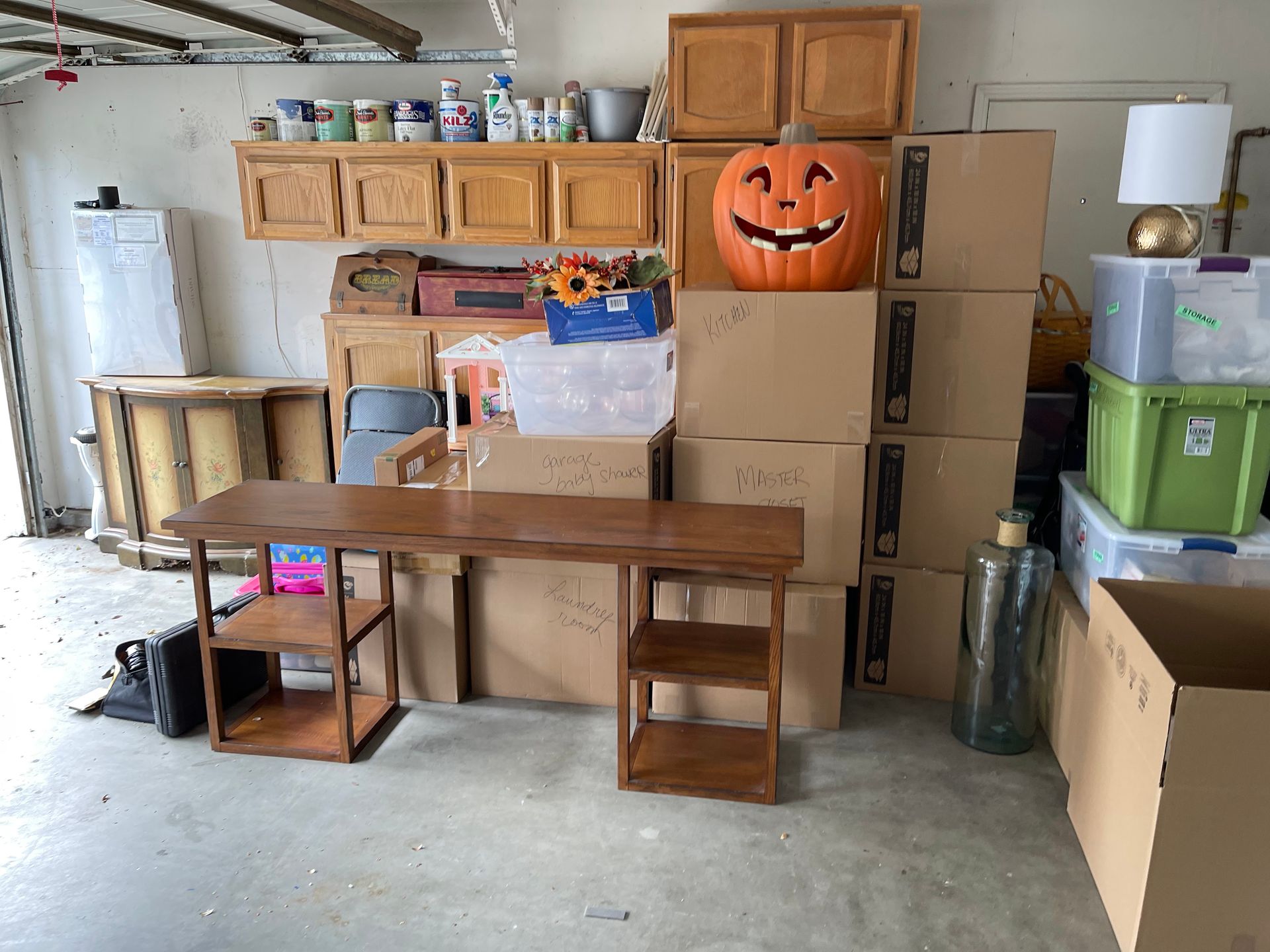 Garage packed with stacked moving boxes, a wooden desk, and a jack-o'-lantern storage bin