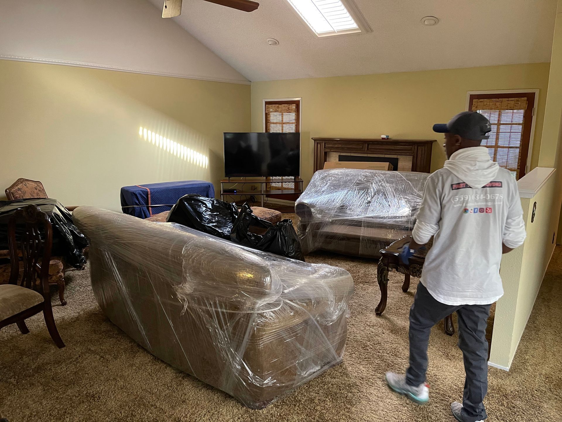 Person wrapping furniture in a living room with plastic during a move or renovation.