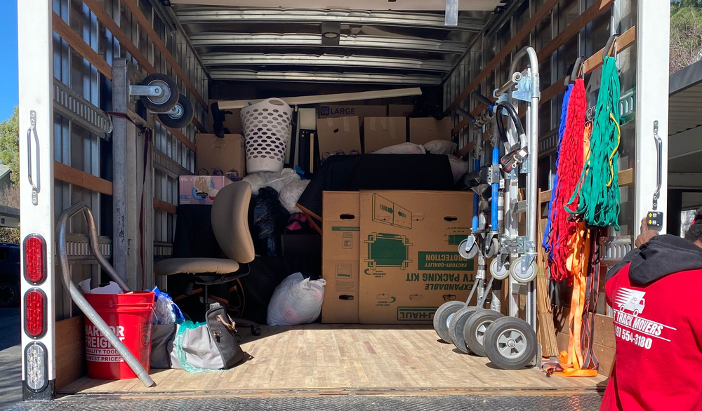 Open moving truck packed with boxes, bags, furniture, and hanging clothing during a move