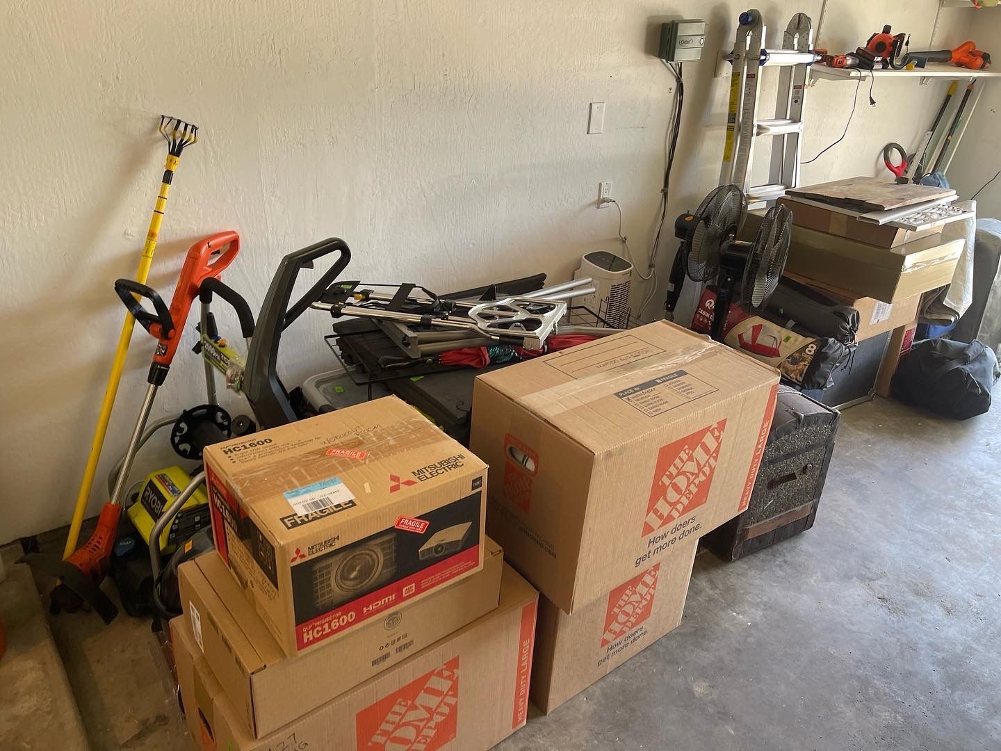 Garage with stacked moving boxes, tools, and equipment along a wall.