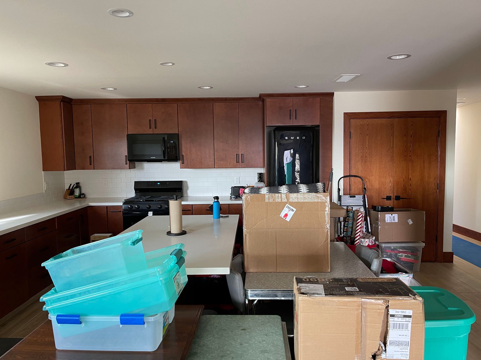 Kitchen packed with moving boxes and storage bins, with cabinets, stove, and refrigerator in the background