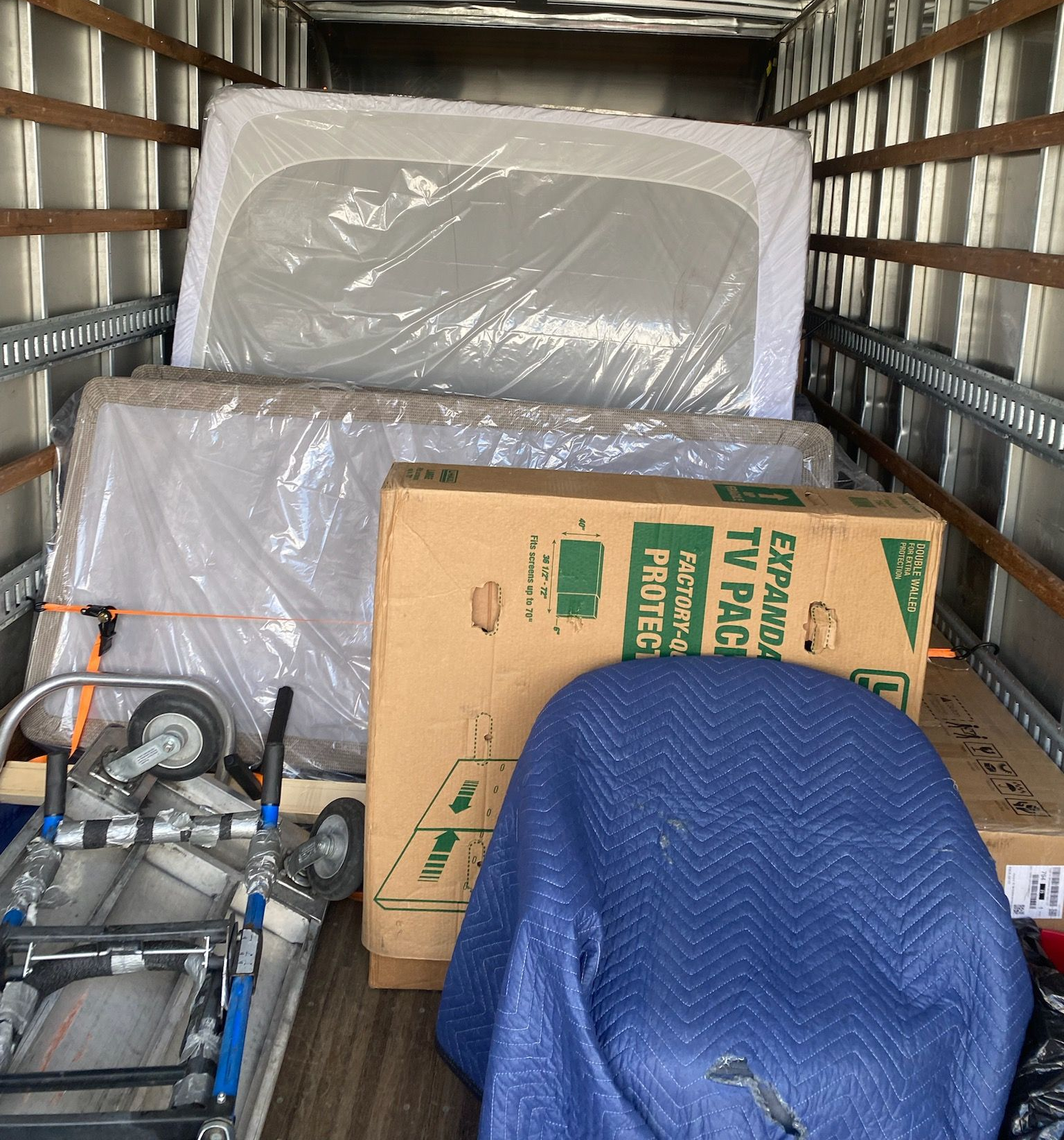 Packed moving truck with wrapped furniture, cardboard boxes, and equipment stacked inside the cargo area.