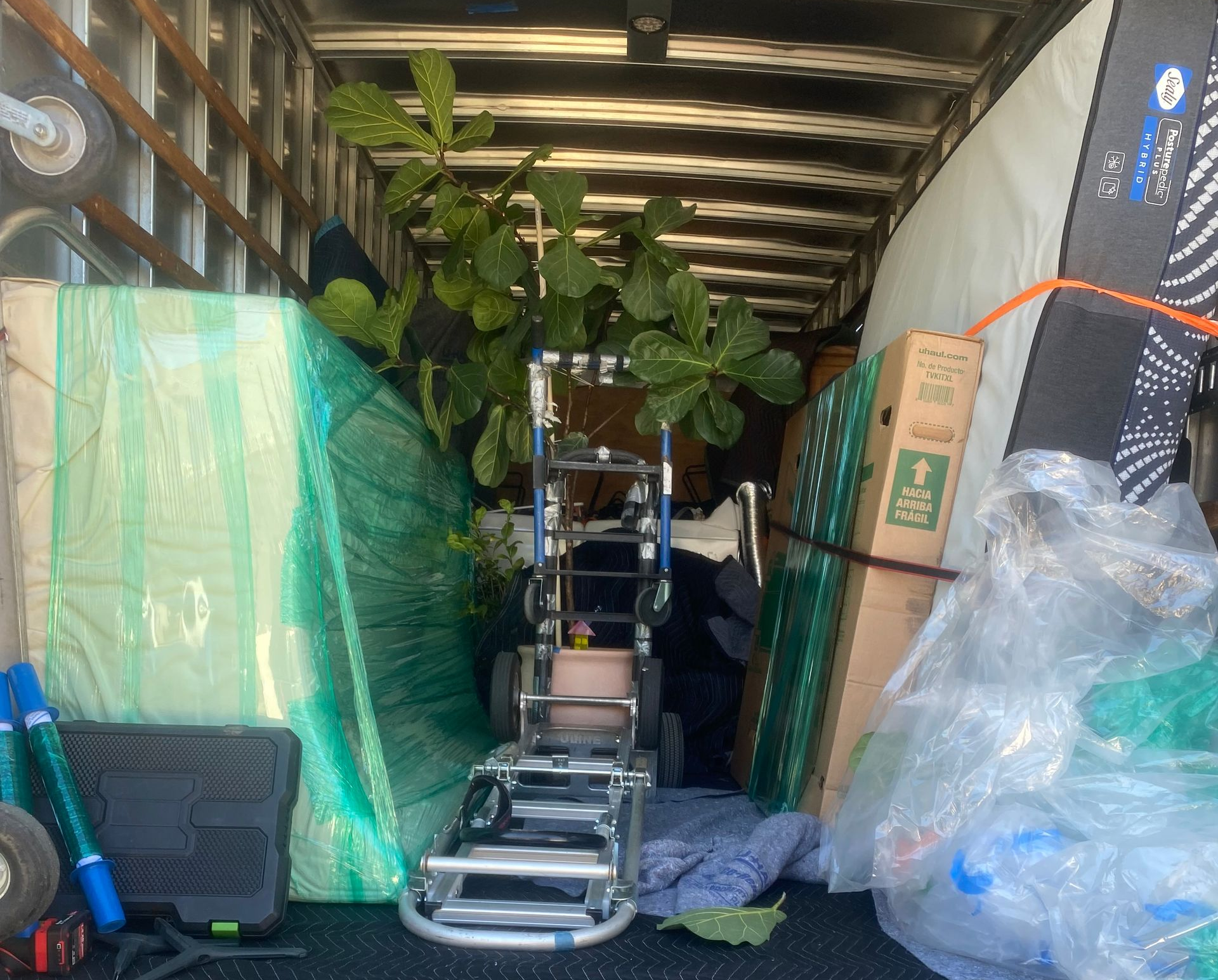 Packed moving truck interior with stacked boxes, plastic-wrapped items, and a dolly carrying a potted plant