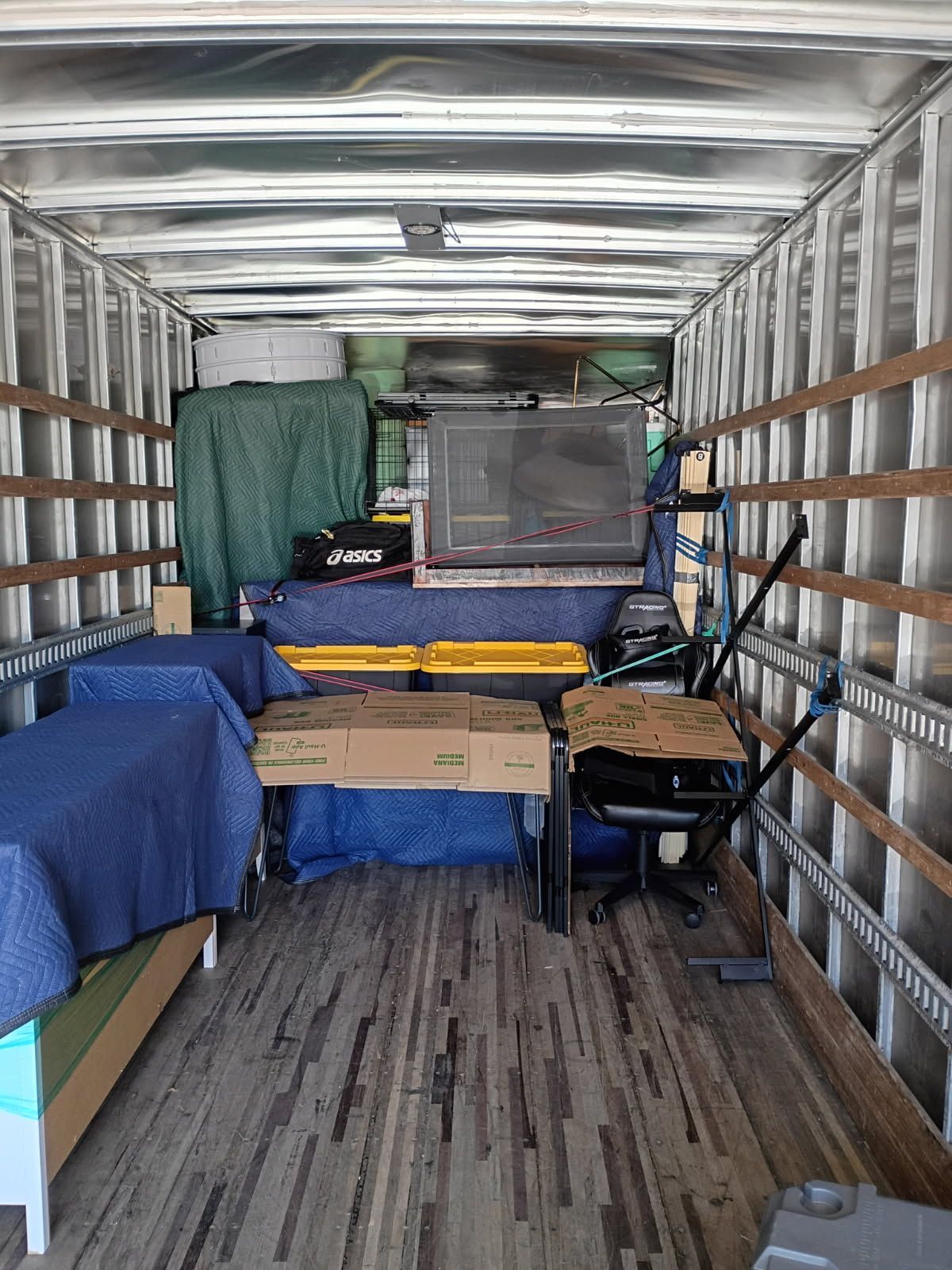 Cargo van interior with a bed, storage bins, table, chair, and covered equipment packed for travel