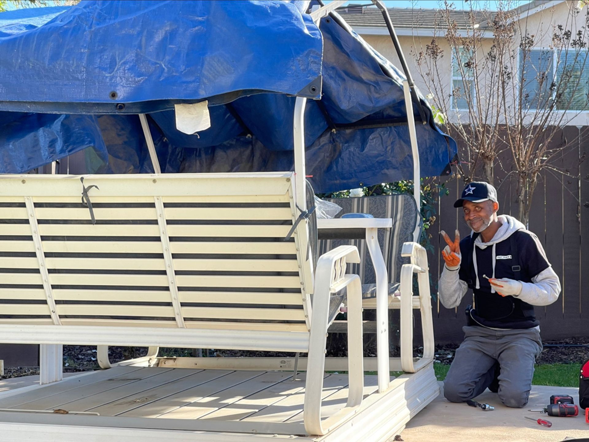 Blue tarp-covered structure with a white bench; a kneeling worker in dark clothing inspects it outdoors.