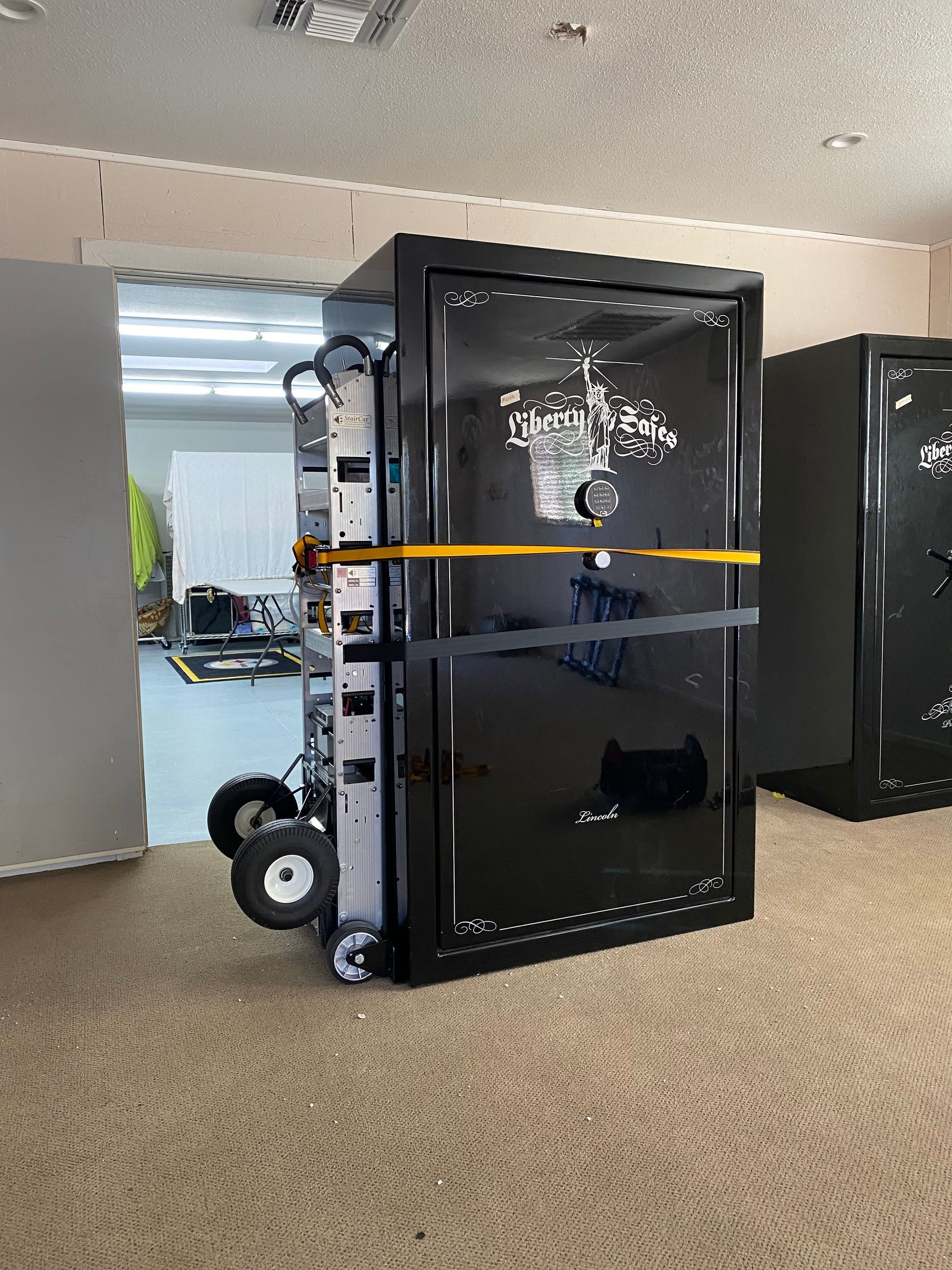 Large black safe being moved on a dolly in an office hallway, secured with a yellow strap.